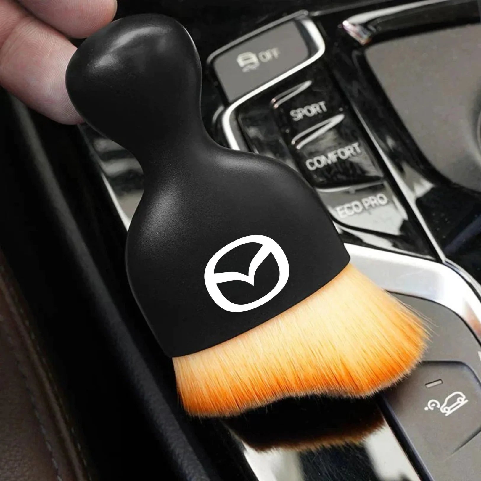 DustMate car detailing brush with the Mazda logo engraved on the handle, held over a car centre console