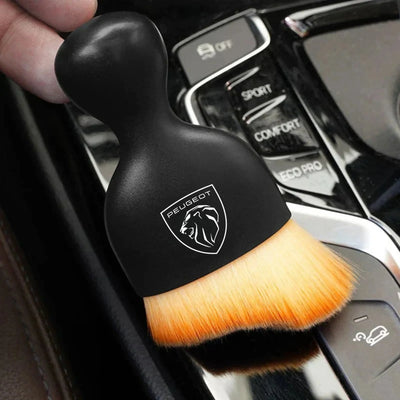 DustMate car detailing brush with the new Peugeot logo engraved on the handle, held over a car centre console