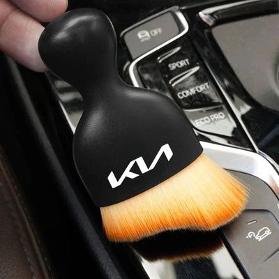 DustMate car detailing brush with the new Kia logo engraved on the handle, held over a car centre console
