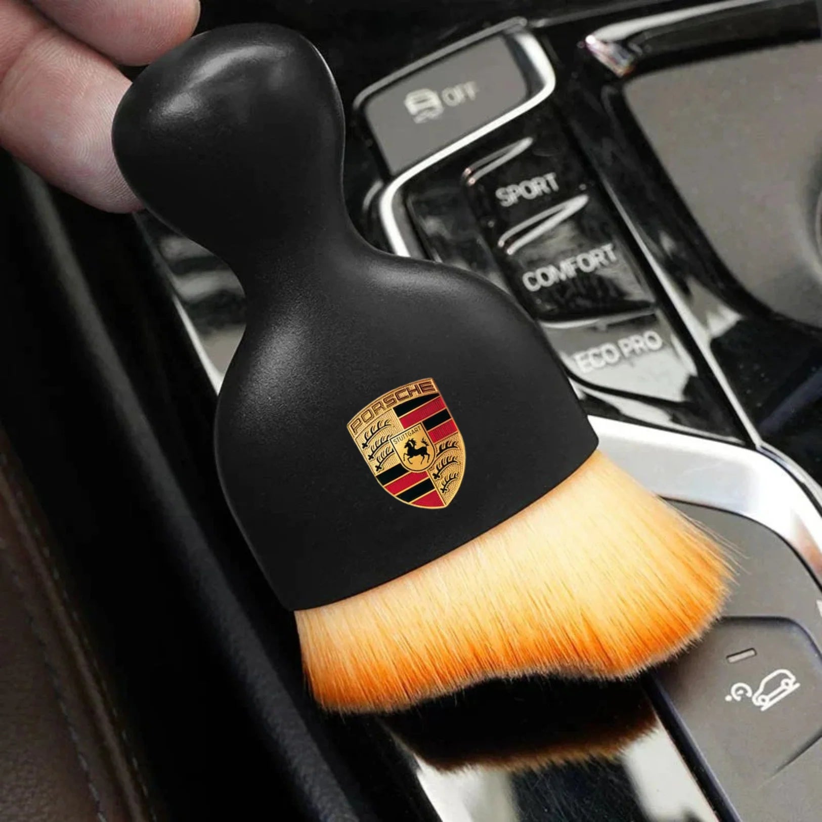 DustMate car detailing brush with the Porsche logo engraved on the handle, held over a car centre console