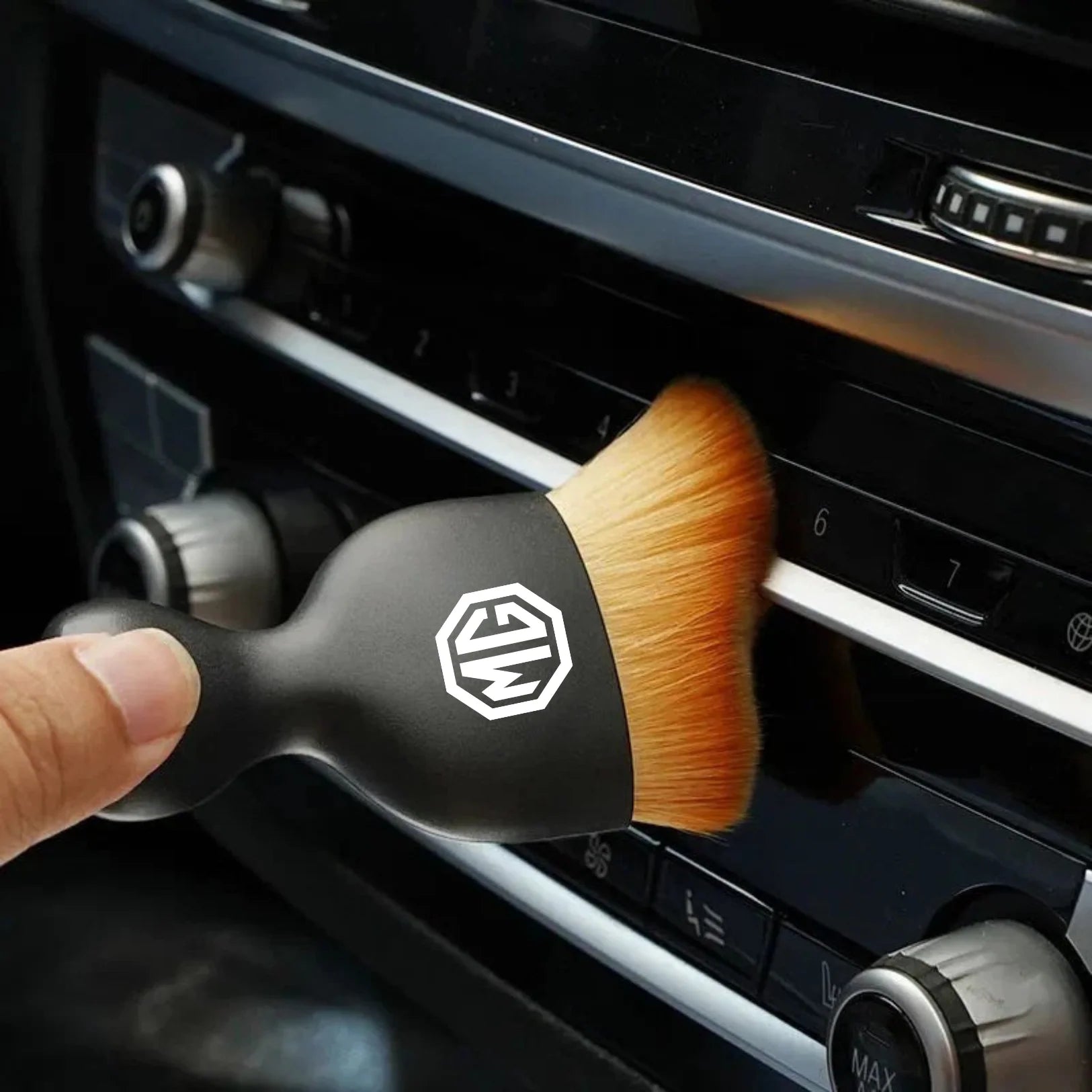 Hand cleaning a car air vent with the DustMate car detailing brush, MG logo engraved on the handle