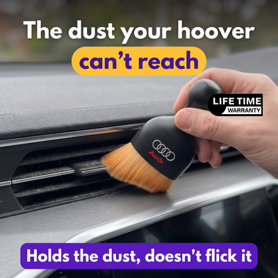 Hand dusting a dashboard air vent with the DustMate car detailing brush, Audi logo engraved on the handle