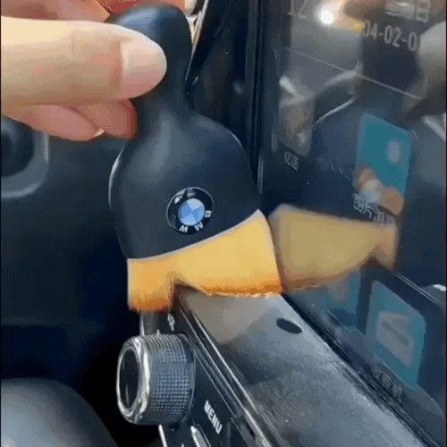 Hand dusting around a car touchscreen with a DustMate car detailing brush, BMW logo engraved on the handle